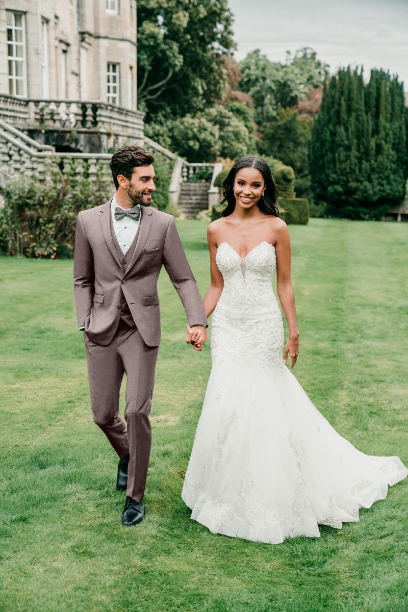 Groom wearing a brown tuxedo holding hands with bride who is wearing a strapless wedding gown